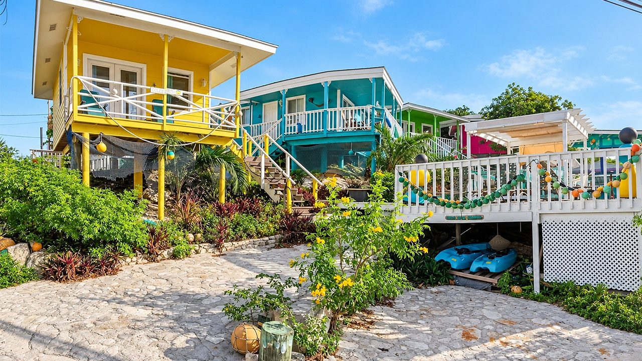 Yellow and teal villas on stilts along a sandy tropical path