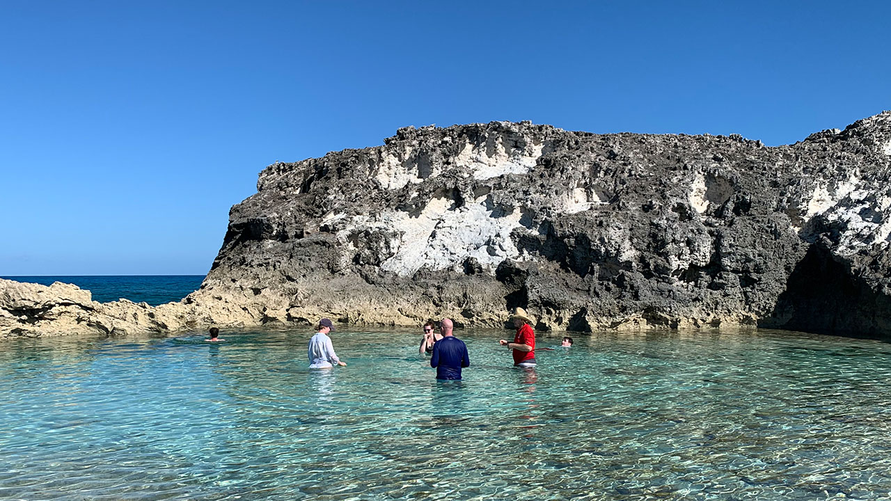 Visitors wading in the natural pool at Rachel's Bubble Bath beneath limestone cliffs
